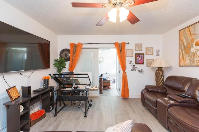 living area with baseboards, light wood-style flooring, a ceiling fan, and a textured ceiling