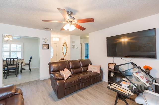 living room featuring a ceiling fan, visible vents, light wood-style flooring, and a textured ceiling