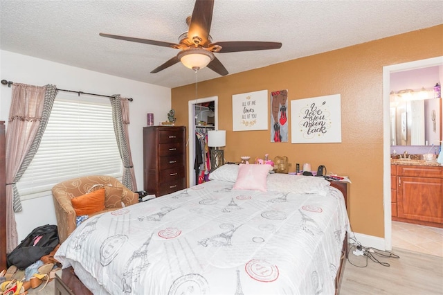 bedroom with ceiling fan, ensuite bathroom, a textured ceiling, light wood-type flooring, and a closet