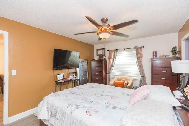 bedroom featuring a textured ceiling, ceiling fan, light wood-style flooring, and baseboards