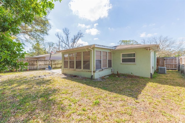 back of house featuring central AC, a lawn, a fenced backyard, and stucco siding