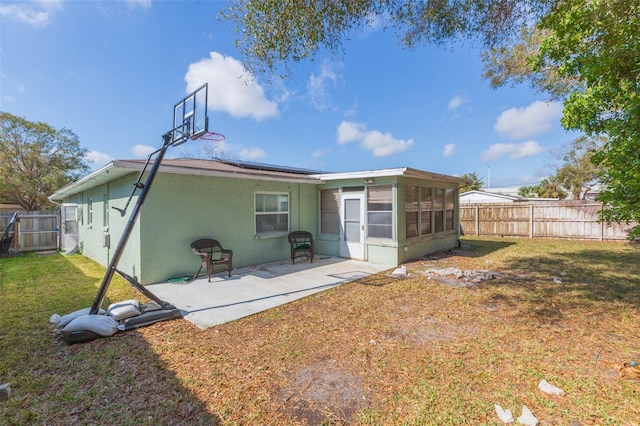 back of property with fence, a sunroom, a lawn, stucco siding, and a patio area