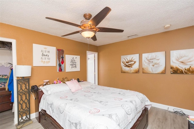 bedroom featuring a textured ceiling, ceiling fan, visible vents, light wood-style floors, and a closet