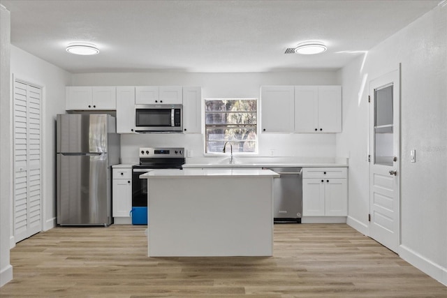 kitchen with stainless steel appliances, white cabinetry, and light hardwood / wood-style floors