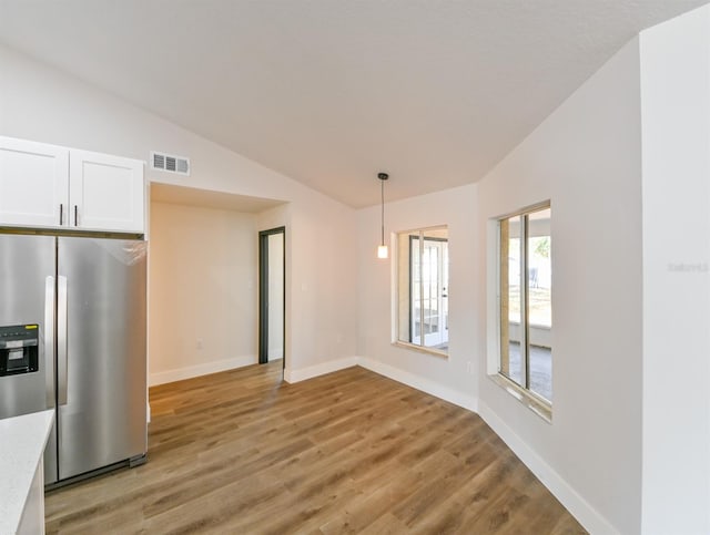 kitchen featuring lofted ceiling, stainless steel fridge with ice dispenser, light hardwood / wood-style flooring, pendant lighting, and white cabinets