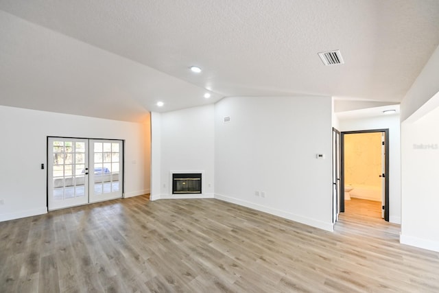 unfurnished living room featuring light hardwood / wood-style flooring, vaulted ceiling, french doors, and a textured ceiling