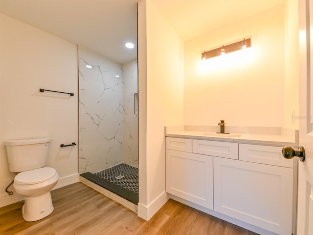 bathroom featuring wood-type flooring, a tile shower, vanity, and toilet