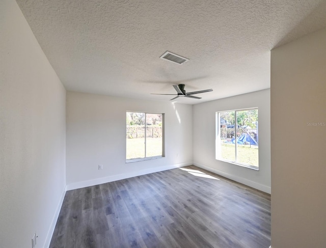 spare room featuring ceiling fan, a healthy amount of sunlight, dark hardwood / wood-style floors, and a textured ceiling