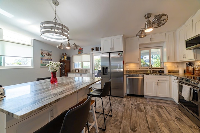 kitchen featuring appliances with stainless steel finishes, white cabinetry, dark hardwood / wood-style flooring, decorative light fixtures, and dark stone counters