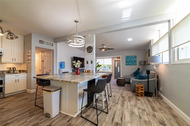 kitchen featuring white cabinetry, a breakfast bar area, light stone counters, and decorative light fixtures