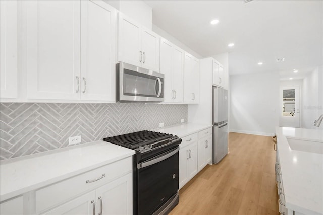 kitchen with appliances with stainless steel finishes, tasteful backsplash, white cabinetry, sink, and light hardwood / wood-style floors