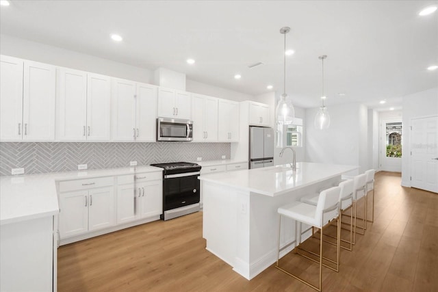 kitchen with pendant lighting, sink, an island with sink, white cabinets, and gas range