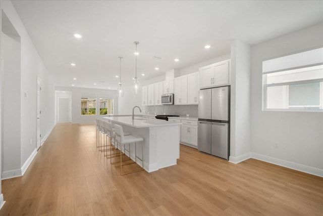 kitchen with stainless steel appliances, white cabinetry, hanging light fixtures, and an island with sink