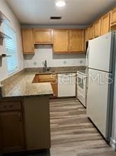 kitchen featuring sink, light stone counters, kitchen peninsula, white appliances, and hardwood / wood-style floors