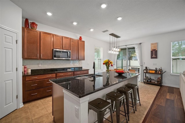 kitchen with pendant lighting, a kitchen breakfast bar, black electric stovetop, a center island with sink, and decorative backsplash