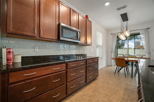 kitchen featuring dark stone countertops, decorative backsplash, light tile patterned flooring, black electric cooktop, and decorative light fixtures