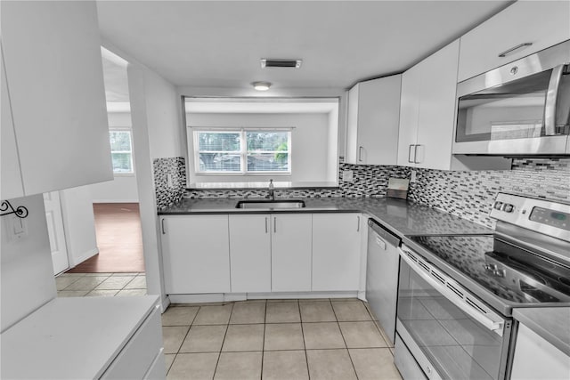 kitchen with sink, light tile patterned floors, appliances with stainless steel finishes, white cabinetry, and backsplash