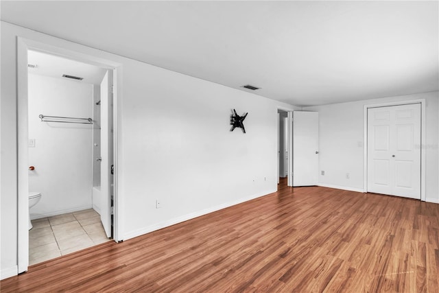 unfurnished bedroom featuring ensuite bathroom and light wood-type flooring