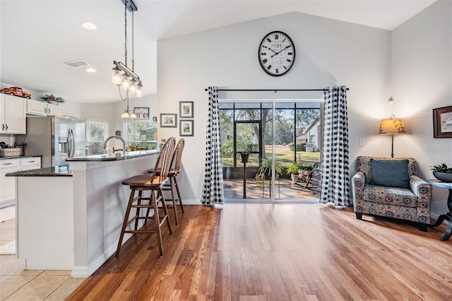 kitchen with hanging light fixtures, plenty of natural light, stainless steel fridge, a kitchen breakfast bar, and white cabinets