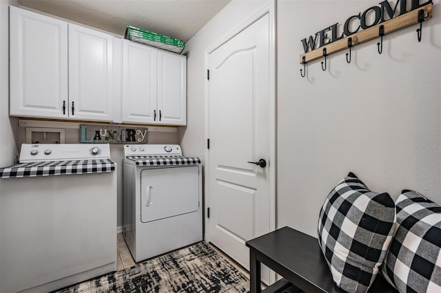 clothes washing area with washing machine and dryer, cabinets, and a textured ceiling