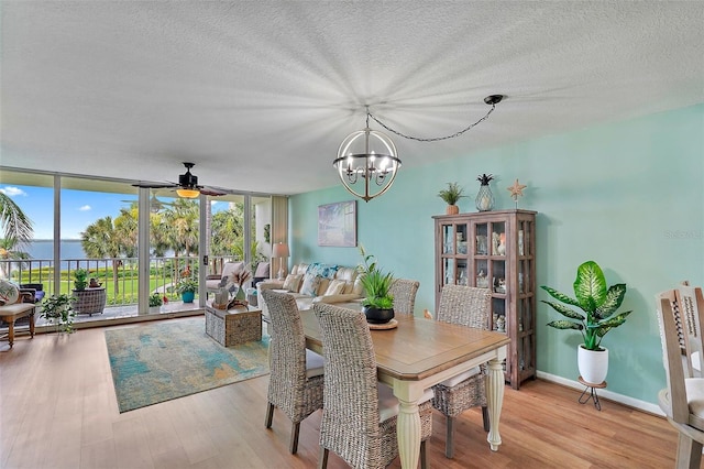 dining room featuring a water view, a textured ceiling, a wall of windows, and light hardwood / wood-style floors