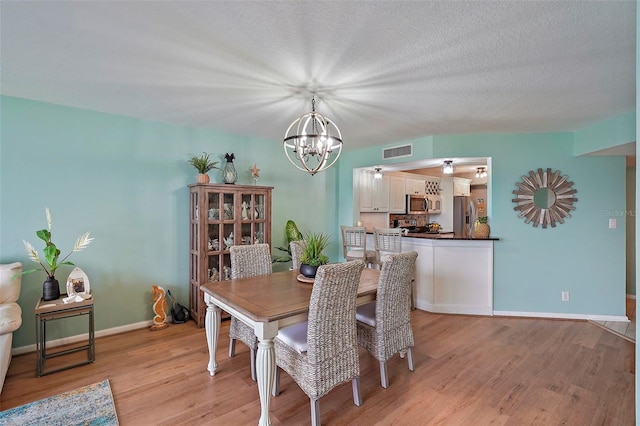 dining area with a chandelier, a textured ceiling, and light hardwood / wood-style floors