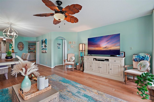 living room featuring ceiling fan with notable chandelier and light hardwood / wood-style flooring