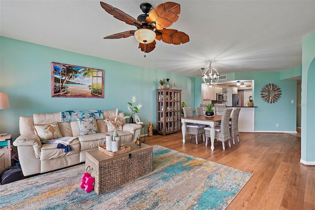 living room featuring ceiling fan with notable chandelier, a textured ceiling, and light wood-type flooring