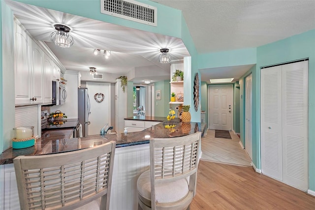 kitchen featuring decorative light fixtures, white cabinets, kitchen peninsula, stainless steel appliances, and light hardwood / wood-style flooring