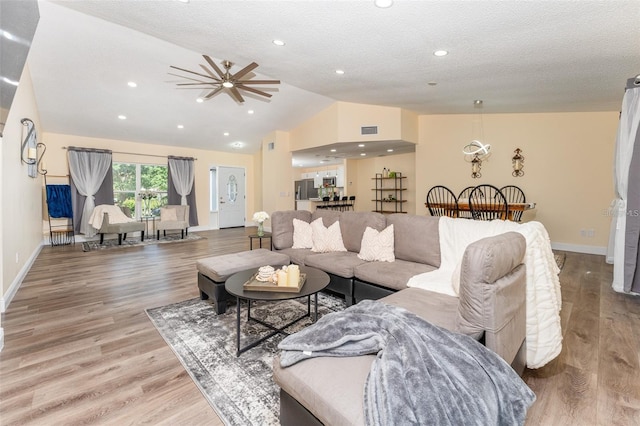 living room featuring vaulted ceiling, a textured ceiling, and light wood-type flooring