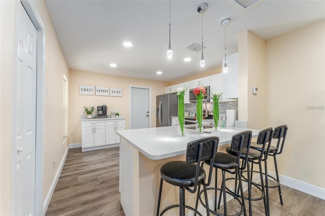 kitchen featuring a kitchen bar, white cabinetry, hanging light fixtures, appliances with stainless steel finishes, and hardwood / wood-style flooring