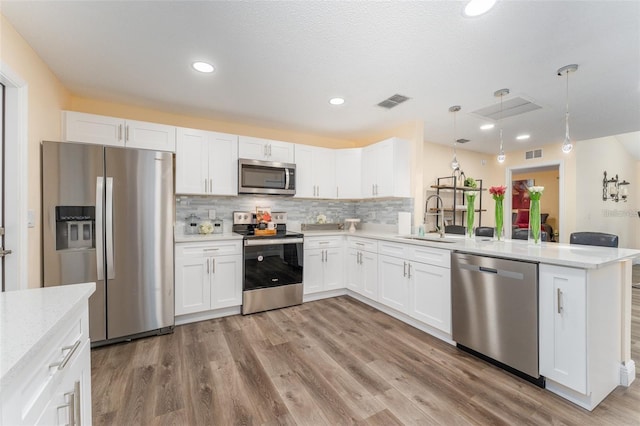 kitchen featuring sink, white cabinetry, kitchen peninsula, pendant lighting, and stainless steel appliances