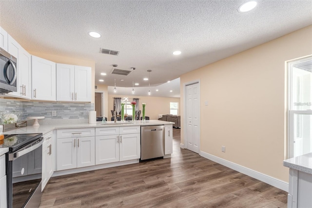 kitchen with dark wood-type flooring, appliances with stainless steel finishes, tasteful backsplash, white cabinets, and kitchen peninsula