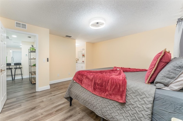 bedroom with ensuite bathroom, a textured ceiling, and light wood-type flooring