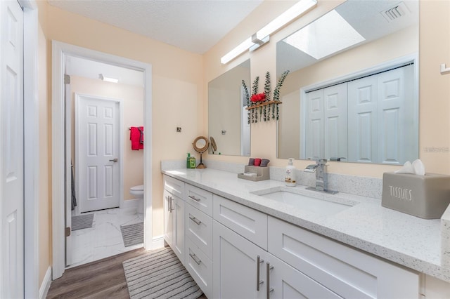 bathroom featuring toilet, a skylight, a textured ceiling, vanity, and hardwood / wood-style flooring