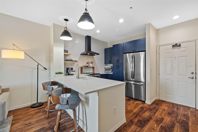 kitchen featuring blue cabinetry, stainless steel refrigerator, a kitchen bar, kitchen peninsula, and wall chimney exhaust hood