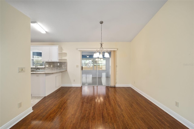 unfurnished dining area featuring lofted ceiling, dark wood-type flooring, sink, and an inviting chandelier