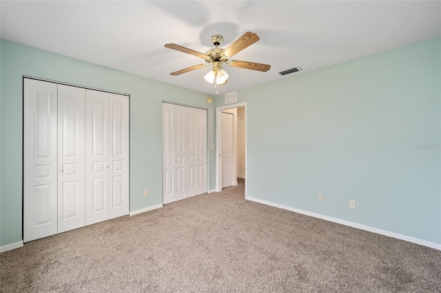 unfurnished bedroom with ceiling fan, multiple closets, and carpet