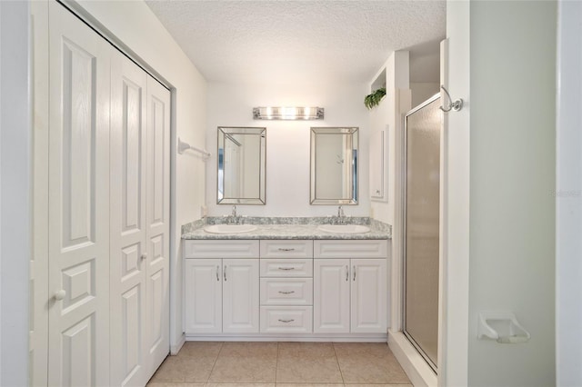 bathroom featuring tile patterned floors, a shower with door, vanity, and a textured ceiling