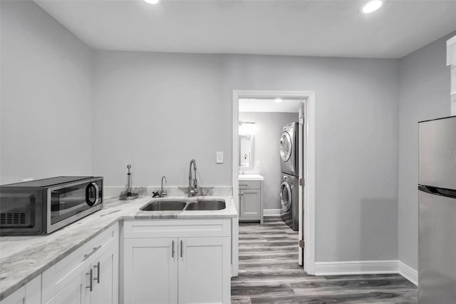 kitchen featuring sink, appliances with stainless steel finishes, stacked washer / dryer, light stone countertops, and white cabinets