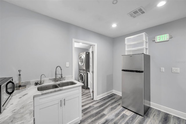 kitchen featuring sink, light stone counters, stainless steel fridge, stacked washer / dryer, and white cabinets