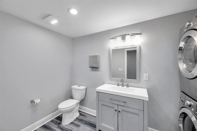 bathroom with stacked washer / dryer, vanity, hardwood / wood-style flooring, and toilet