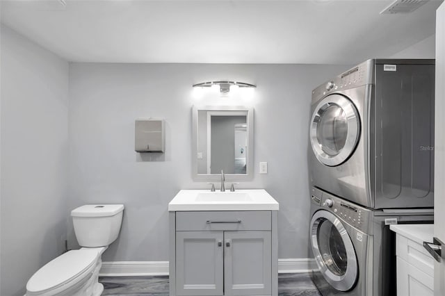 laundry area featuring stacked washer / drying machine, dark wood-type flooring, and sink