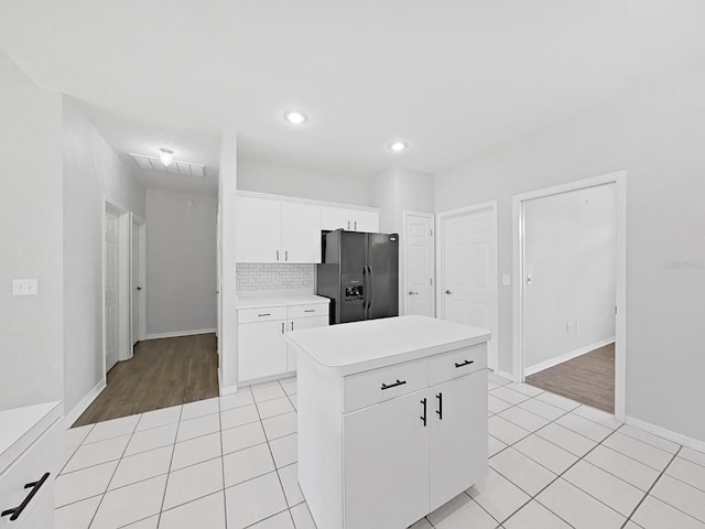 kitchen featuring a kitchen island, light tile patterned floors, white cabinets, and black refrigerator with ice dispenser