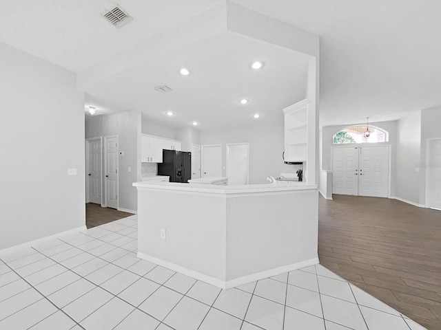 kitchen featuring light hardwood / wood-style flooring, white cabinets, black fridge with ice dispenser, and kitchen peninsula