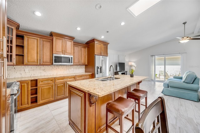 kitchen featuring appliances with stainless steel finishes, sink, a breakfast bar area, light stone counters, and a center island with sink