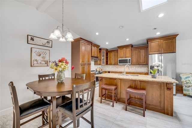 kitchen featuring sink, decorative light fixtures, a center island with sink, appliances with stainless steel finishes, and light stone countertops