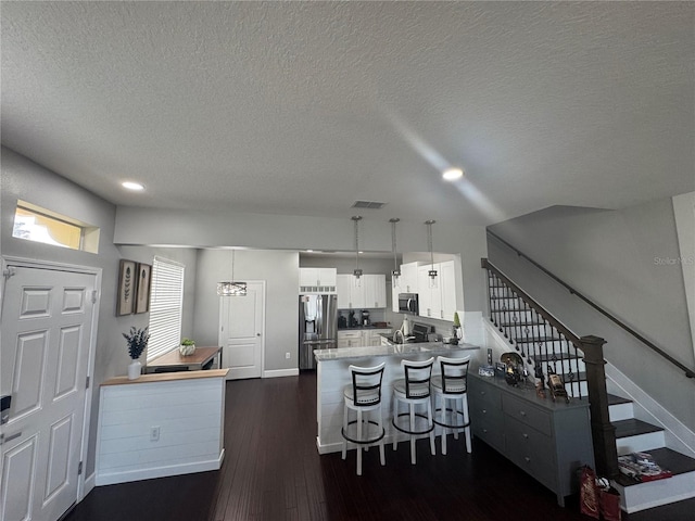 kitchen with appliances with stainless steel finishes, white cabinetry, a kitchen breakfast bar, hanging light fixtures, and kitchen peninsula