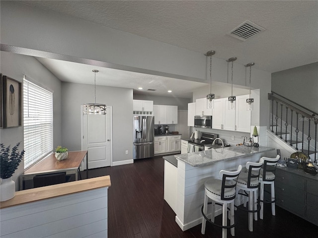 kitchen featuring appliances with stainless steel finishes, a breakfast bar, pendant lighting, white cabinetry, and kitchen peninsula