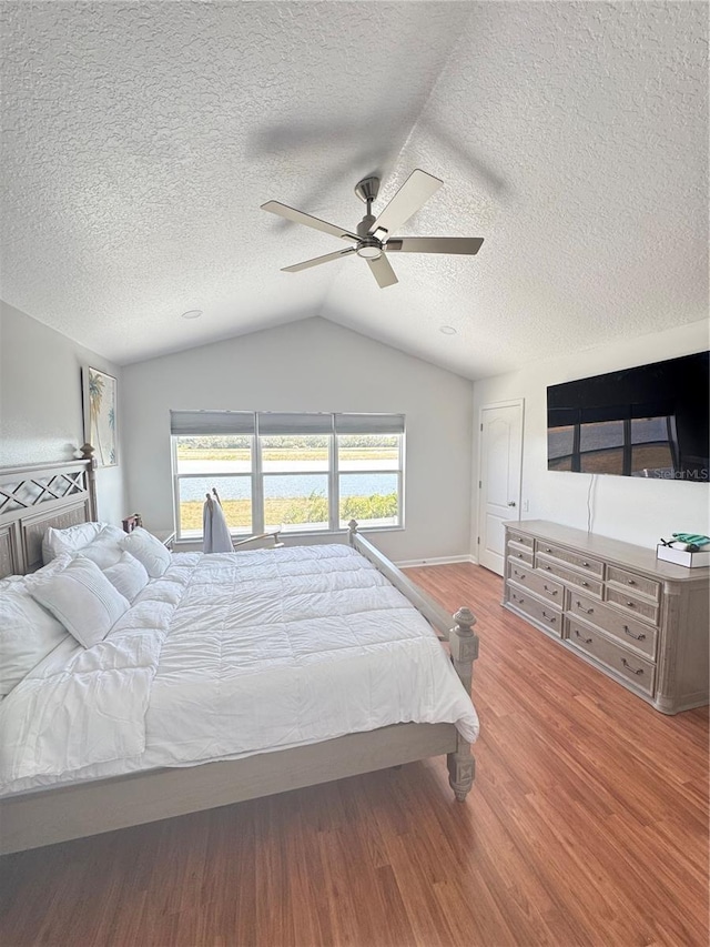 bedroom featuring ceiling fan, lofted ceiling, wood-type flooring, and a textured ceiling